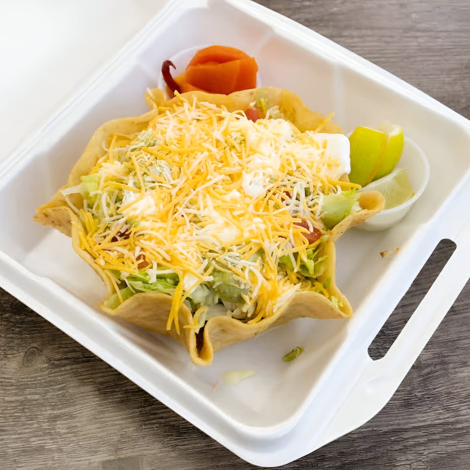 A taco salad in a crispy tortilla bowl, topped with shredded cheese, lettuce, and sour cream.