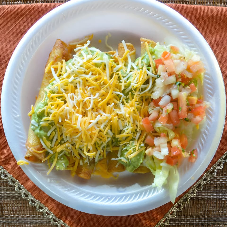 Oscar's Taco Shop taquitos topped with guacamole, shredded cheese, lettuce, and pico de gallo.