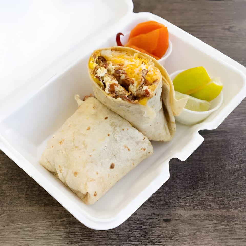 Two Oscar's Taco Shop burritos in a white takeout container with lime wedges and pickled carrots.