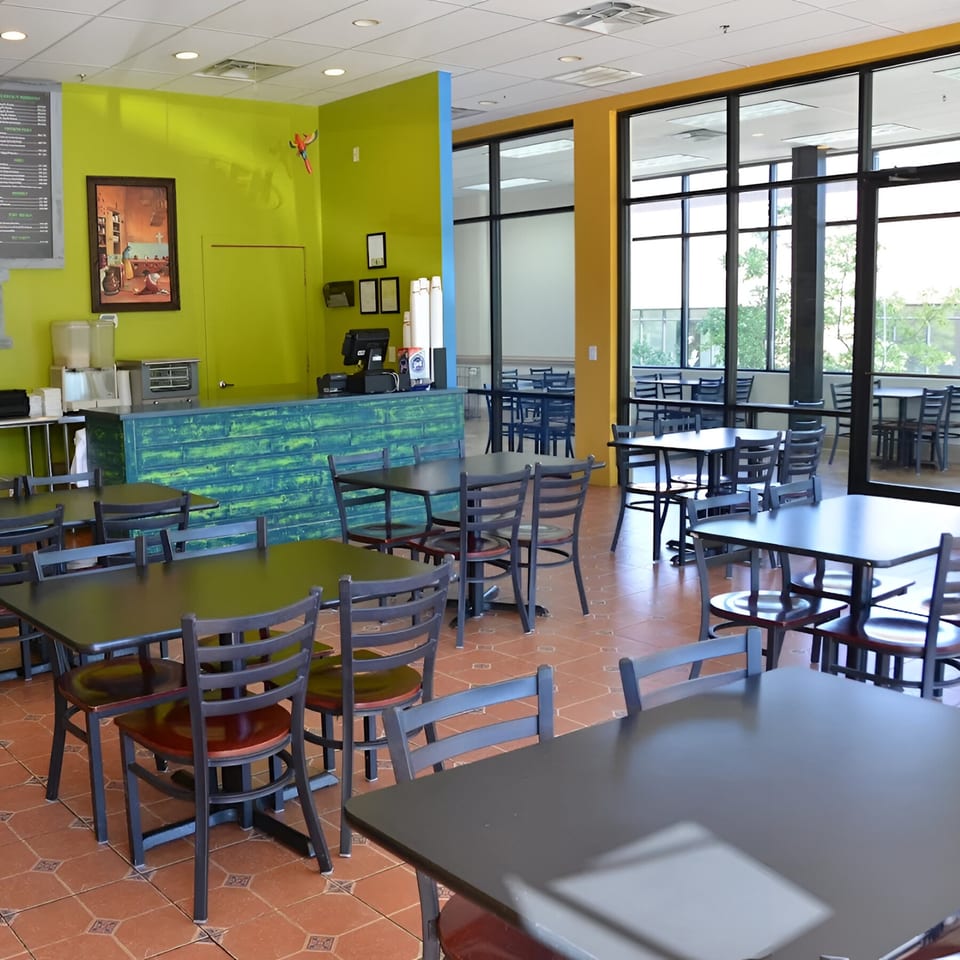 Interior of Oscar's Taco Shop with lime green walls, black tables, and large windows.