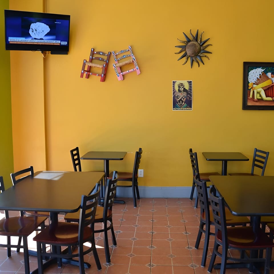 Interior of Oscar's Taco Shop with yellow walls, dark tables and chairs, and Mexican-themed decor.