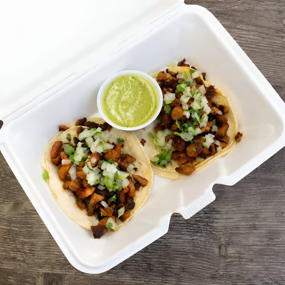 Two Oscar's Taco Shop tacos with meat, onions, cilantro, and a side of green salsa.