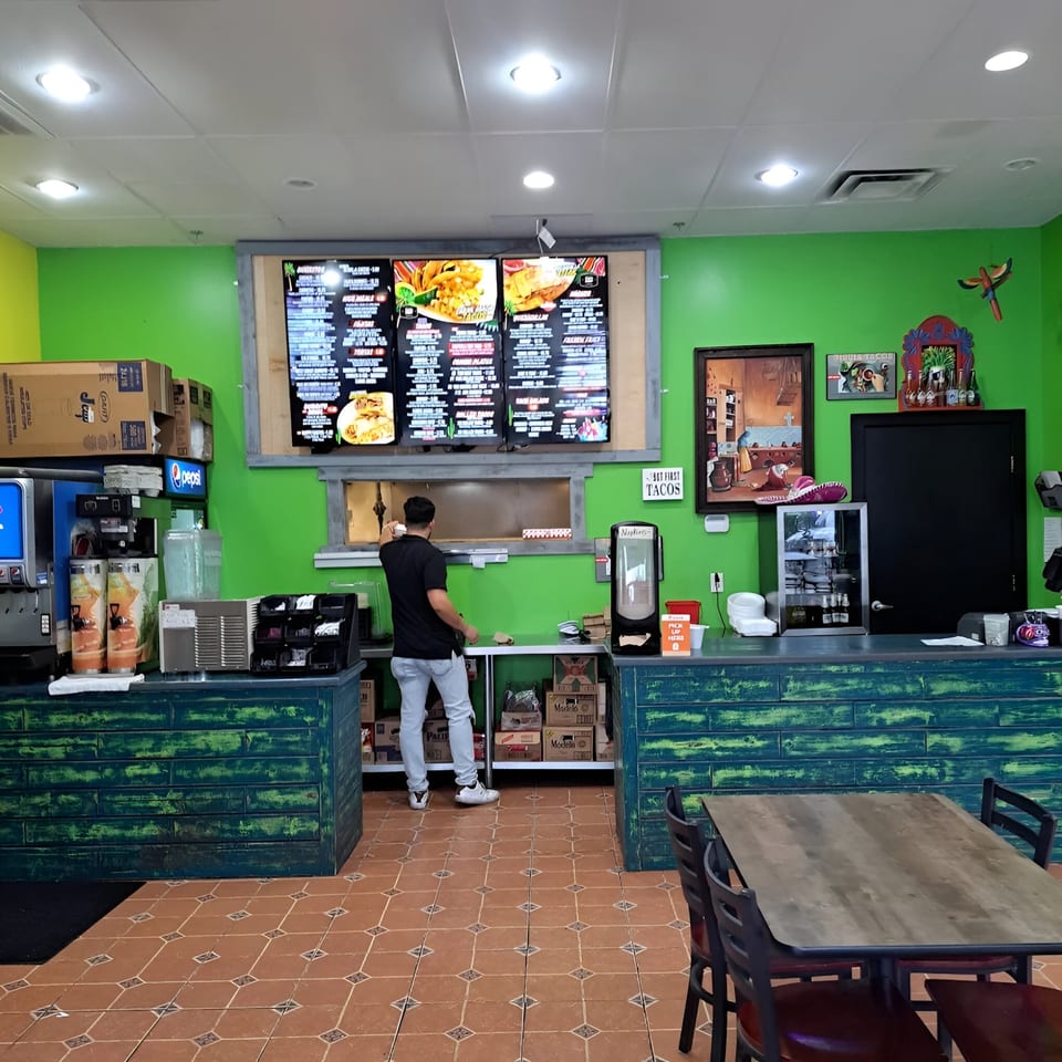 A man stands behind a counter in Oscar's Taco Shop, with a large menu board above him.