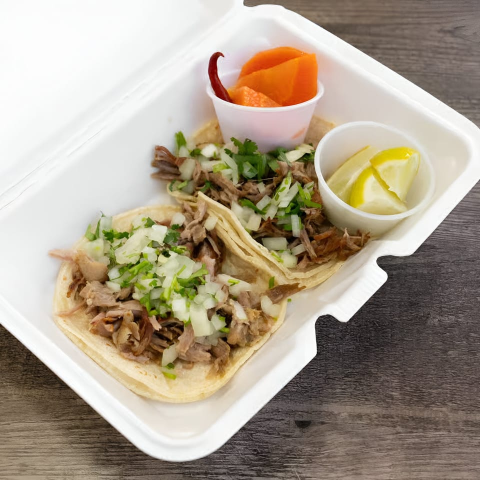 Two Oscar's Taco Shop tacos with meat, onions, cilantro, and sides of lemon and carrots.